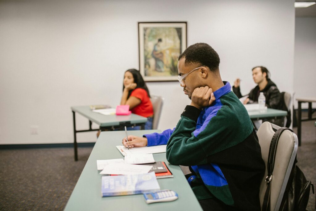 University students focused and studying during an exam, surrounded by desks and study material in a classroom setting.